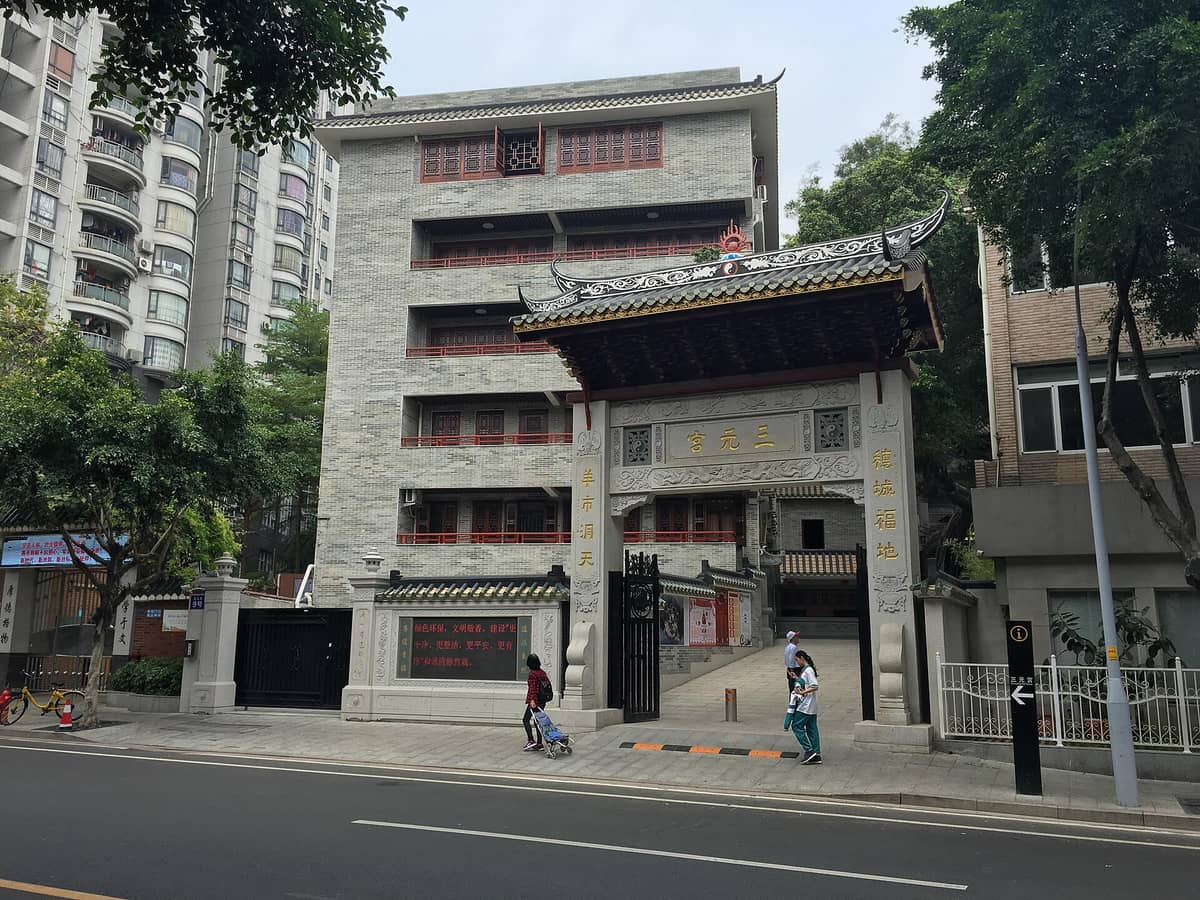 Street view of the Sanyuan Palace entrance gate in Guangzhou, showing traditional Chinese architecture set among modern city buildings.