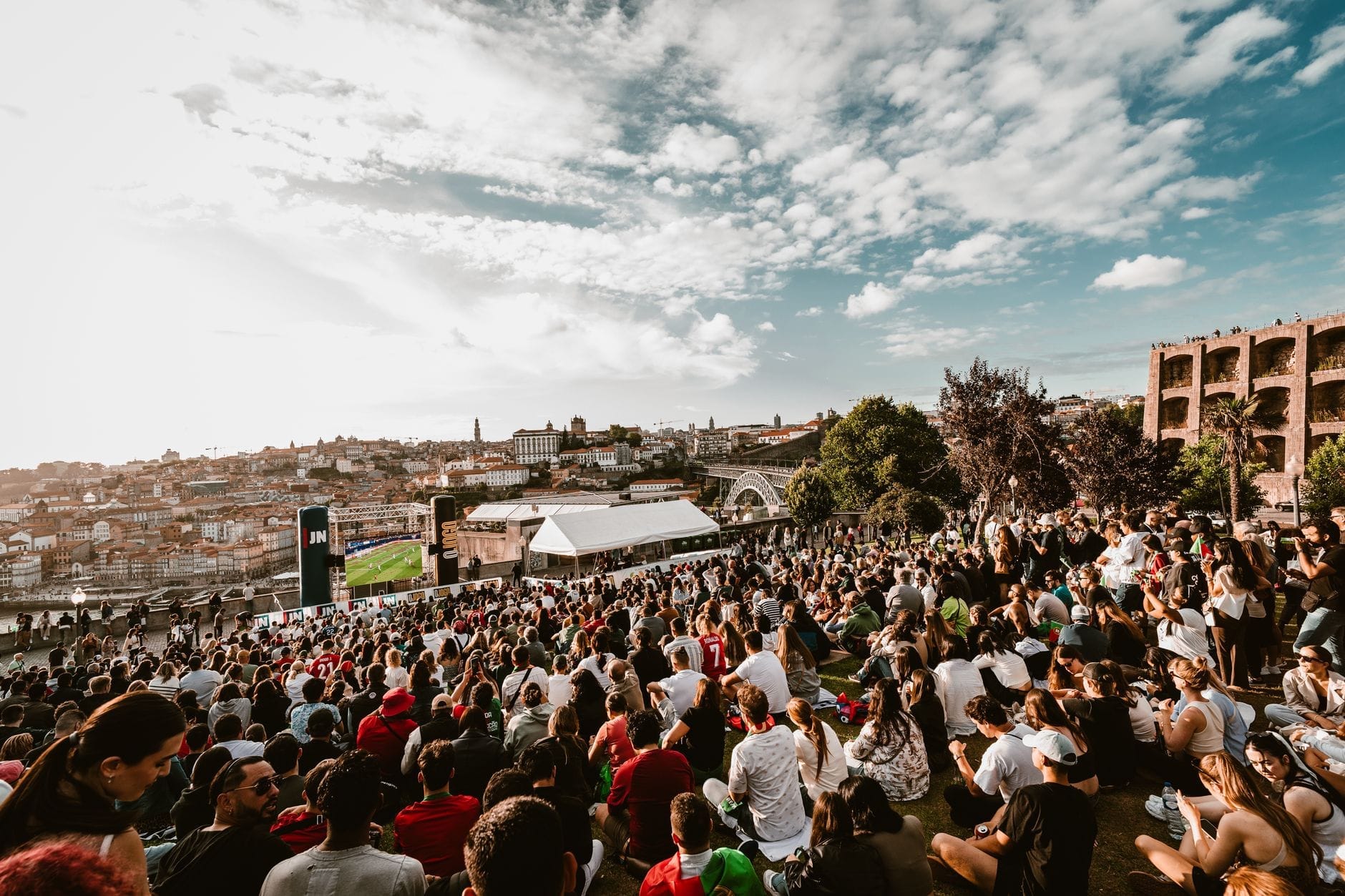 Grande multidão reunida em uma colina com vista para o Porto em clima de festa, skyline da cidade e céu dramático — a energia do Festival de São João em todo o seu esplendor.
