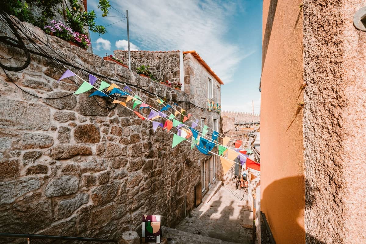 Enge Steinstraße in Porto mit bunten Festgirlanden unter einem strahlend blauen Himmel, die die festliche Atmosphäre von São João einfängt.