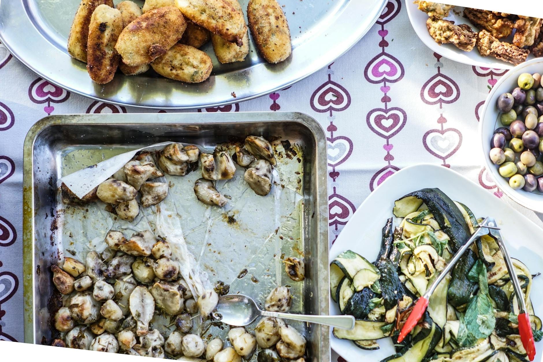 Platten mit rustikalem Hausmannskost, darunter geröstete Kartoffeln, Gnocchi, gegrilltes Gemüse, Oliven und Antipasti auf einem gemusterten Tischtuch, das eine italienische Bauernmahlzeit heraufbeschwört.