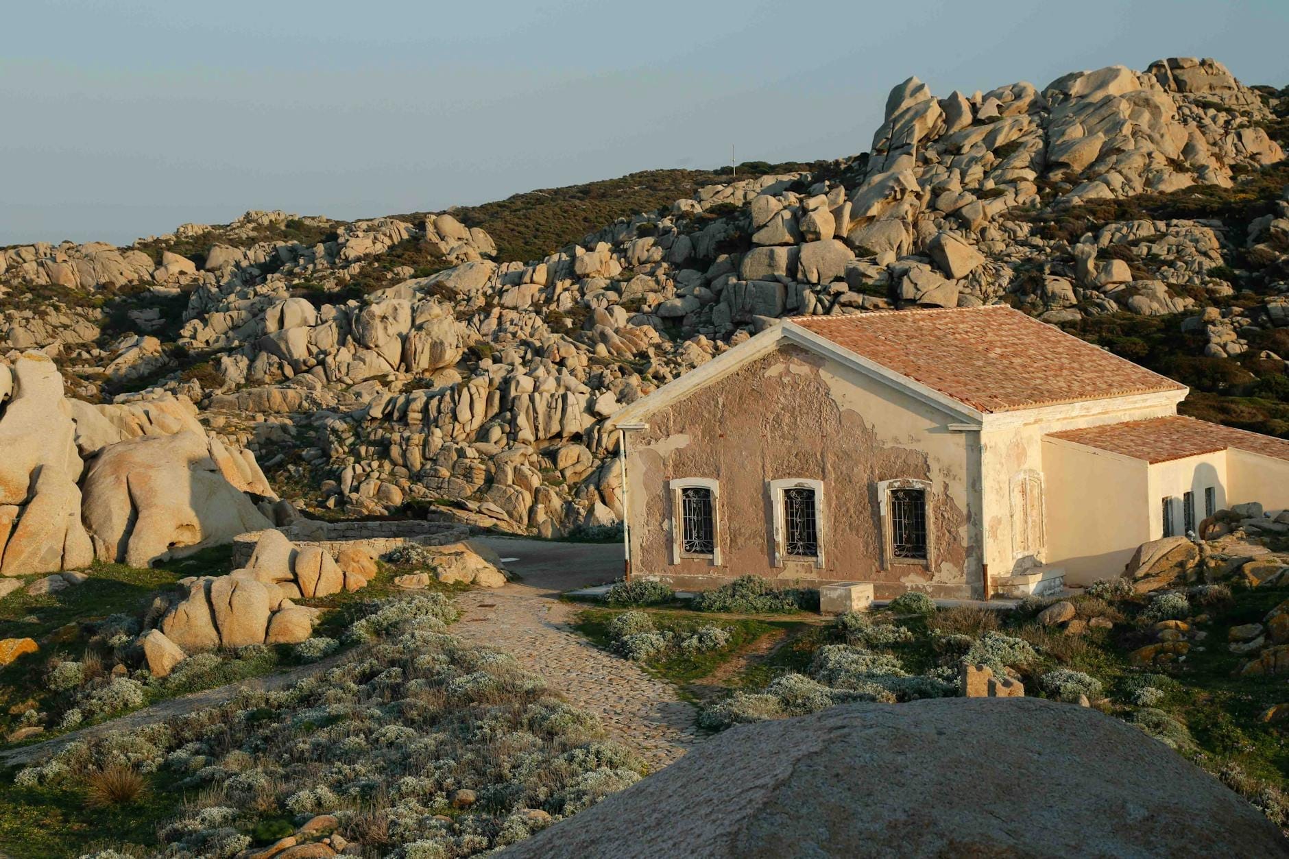 Ein rustikales Steinhaus inmitten rauer Felshügel und karger Vegetation im Inneren Sardiniens – ein Bild traditionellen Dorflebens und zeitloser Kultur.