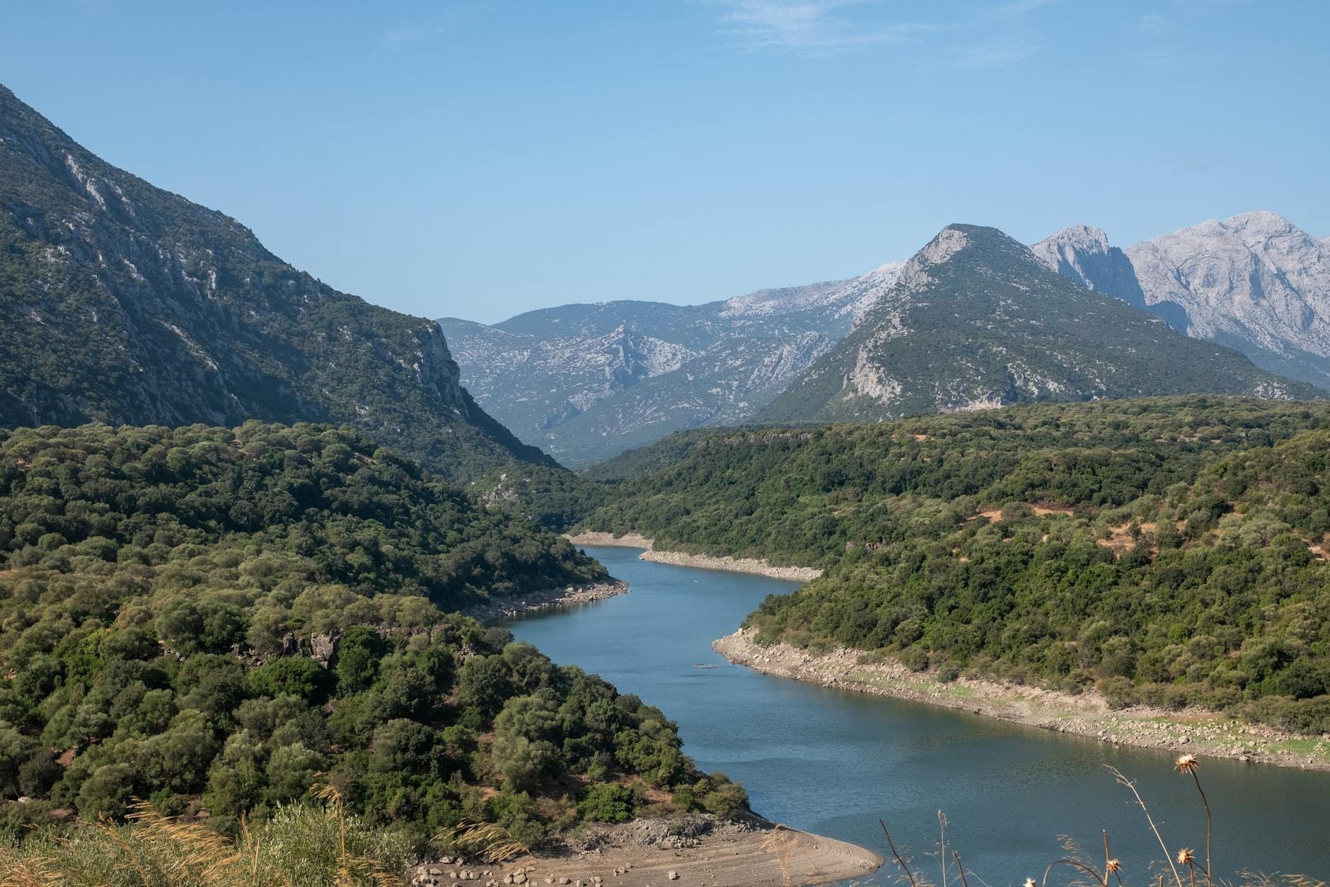 Malerischer Blick auf einen Fluss, der sich durch grüne Hügel und Berge in Sardinien an einem klaren Tag schlängelt