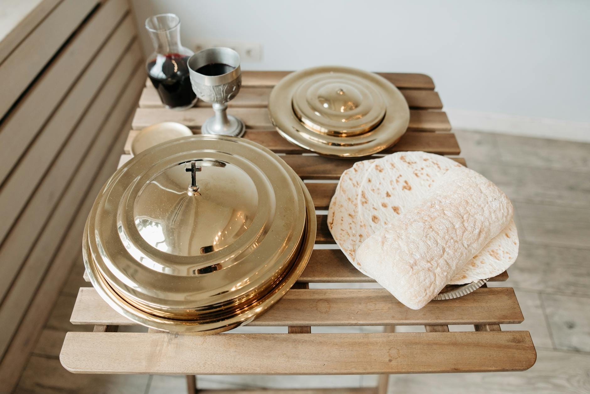 Ein rustikaler Holztisch mit dünnen, runden Fladenbroten, die an Pane carasau erinnern, neben eleganten Metallservierplatten und einem Glas Rotwein.