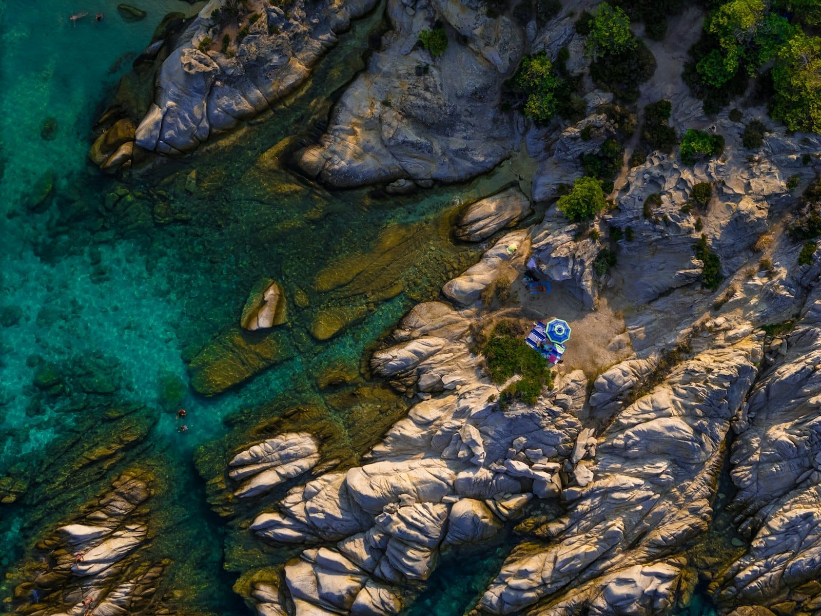 Eine atemberaubende felsige Küste mit klarem türkisfarbenem Wasser, kleinen Sandstreifen und einem Sonnenschirm an einem abgelegenen Platz, der an einen ruhigen, romantischen Strand auf Sardinien erinnert.