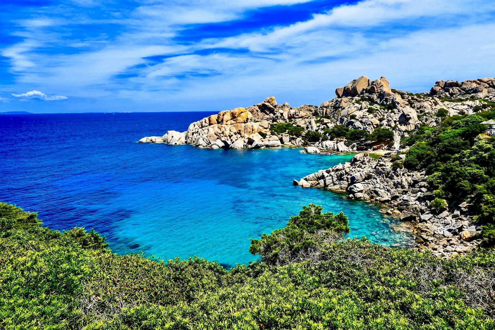 Eine atemberaubende, abgeschiedene Bucht auf Sardinien mit türkisfarbenem Wasser, Felsklippen und üppiger Vegetation unter strahlend blauem Himmel – ideal für Paare.