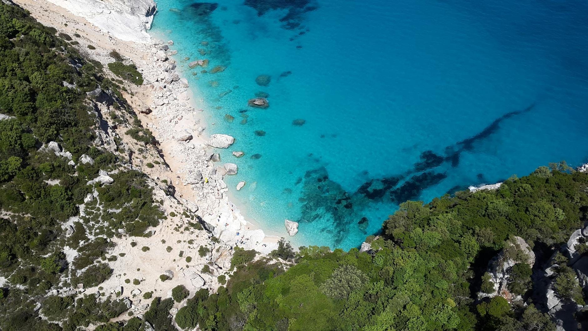 Luftaufnahme eines abgelegenen Strandes auf Sardinien mit türkisfarbenem Wasser, weißem Sand, Felsen und üppigem Grün entlang der Küste