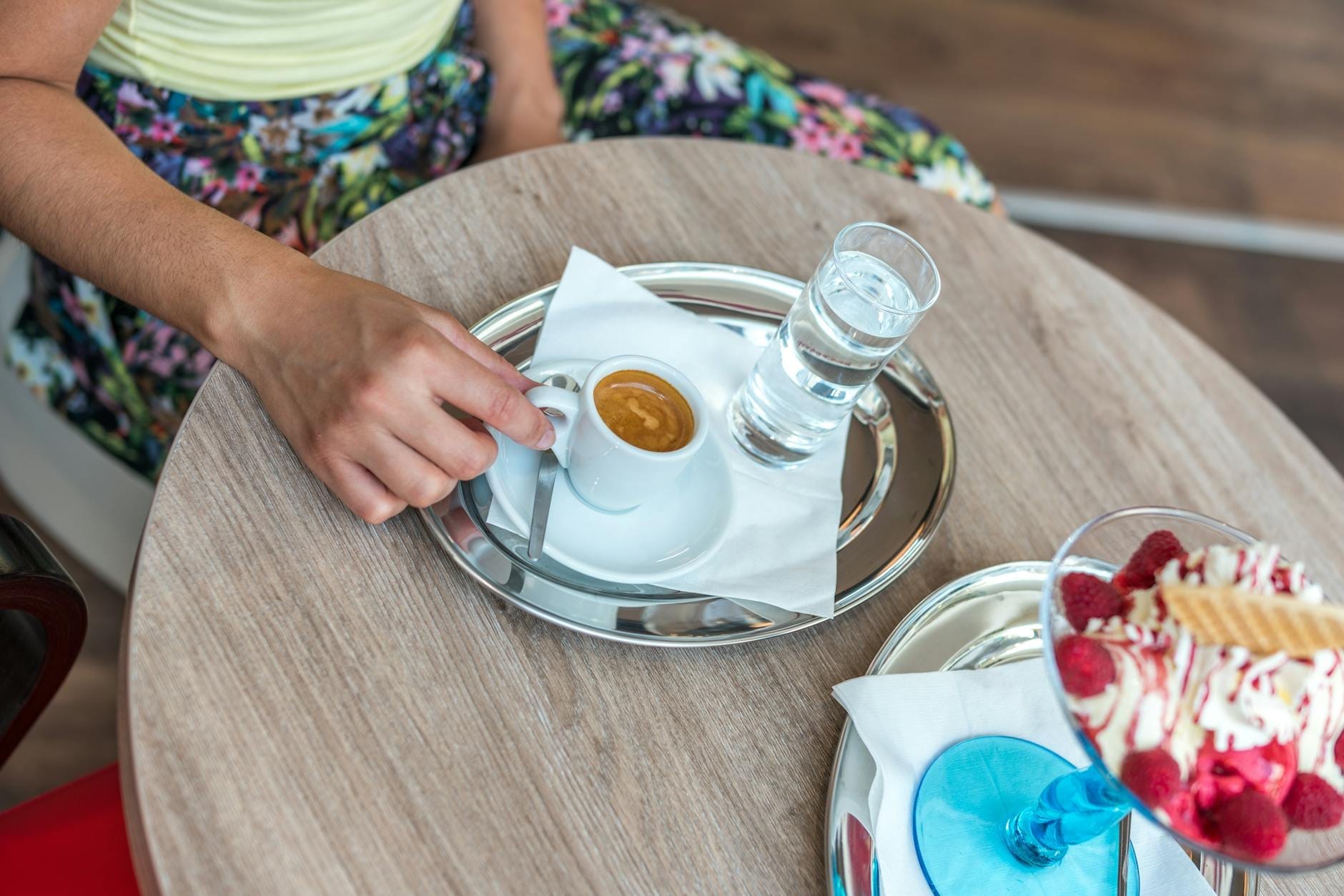 Eine Person an einem Café-Tisch, die einen Espresso mit einem Glas Wasser und einem Dessert hält, und die italienische Café-Kultur heraufbeschwört.