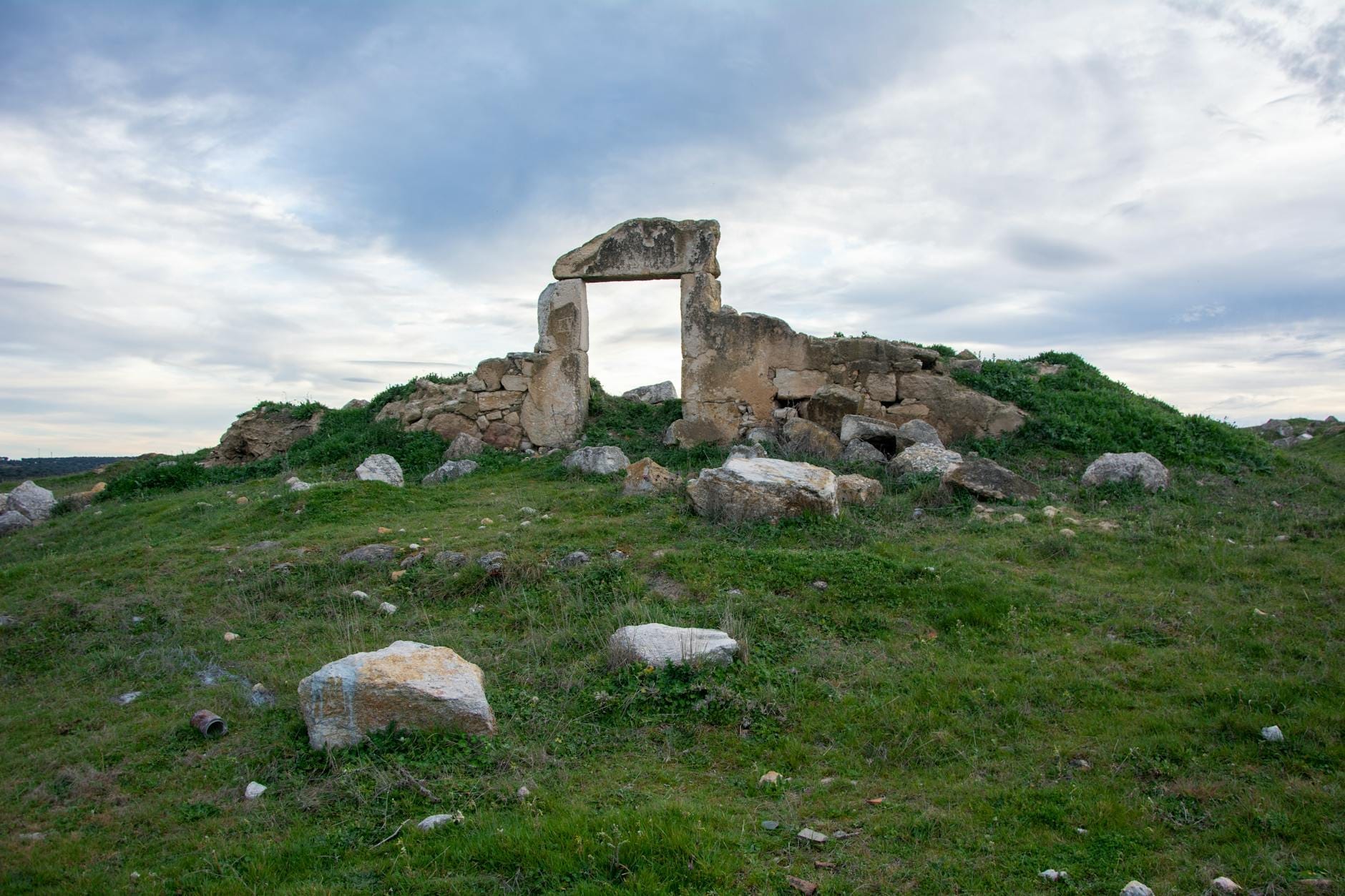 Antike steinerne Grabstruktur mit aufrechten und waagerechten Platten in einer Graslandschaft unter bewölktem Himmel in Sardinien.