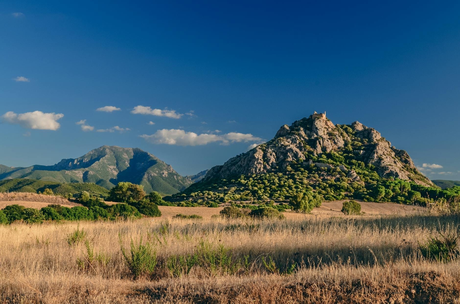Felsiger Hügel in einer ländlichen sardischen Landschaft mit antiken Ruinen auf dem Gipfel unter blauem Himmel.