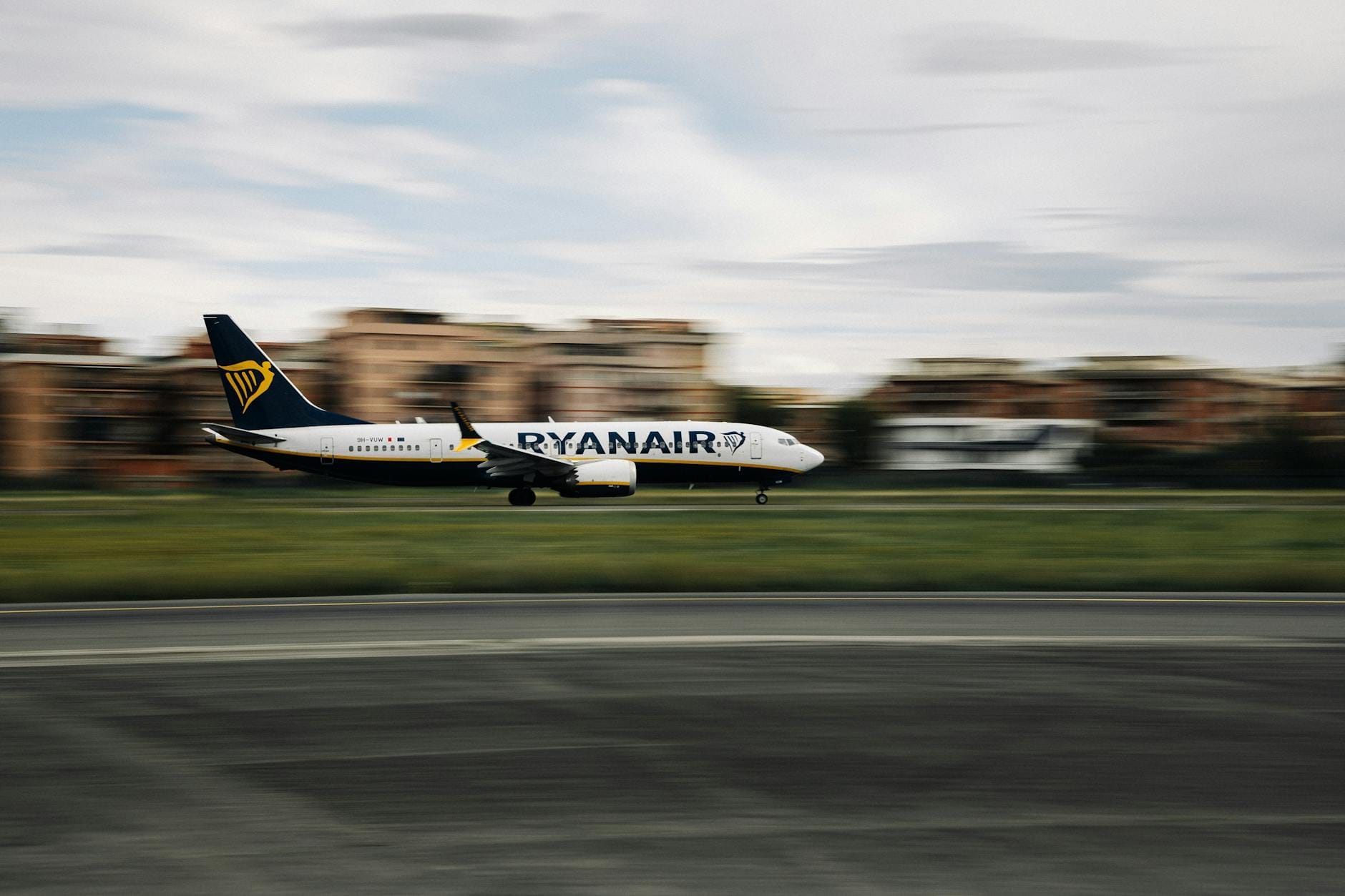 Ein Ryanair-Flugzeug beim Start oder bei der Landung auf einer Landebahn mit verschwommenen Gebäuden im Hintergrund.