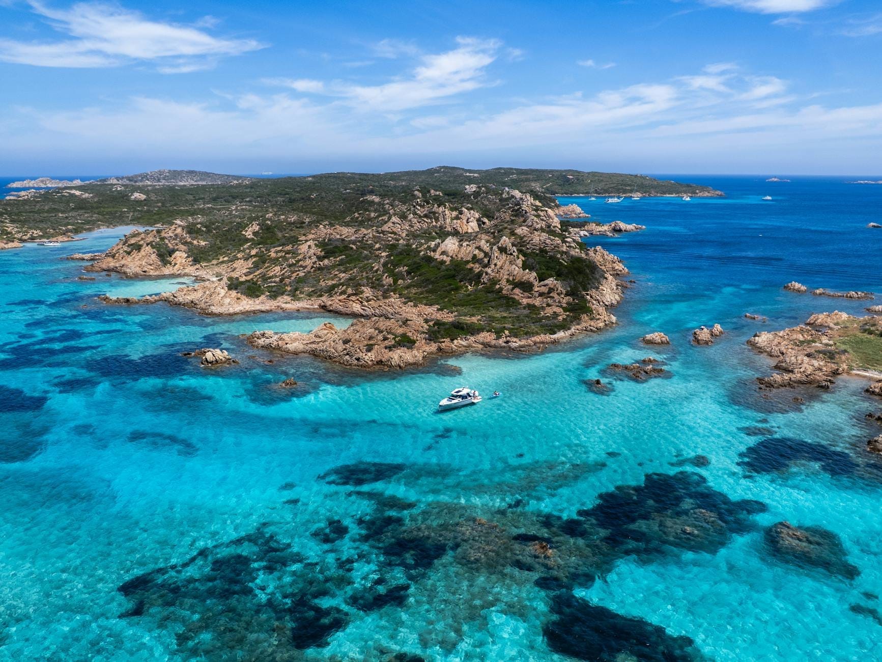 Luftaufnahme des Archipels La Maddalena mit felsigen Inseln, türkisfarbenem Wasser und einem in den klaren Untiefen ankernden Boot.