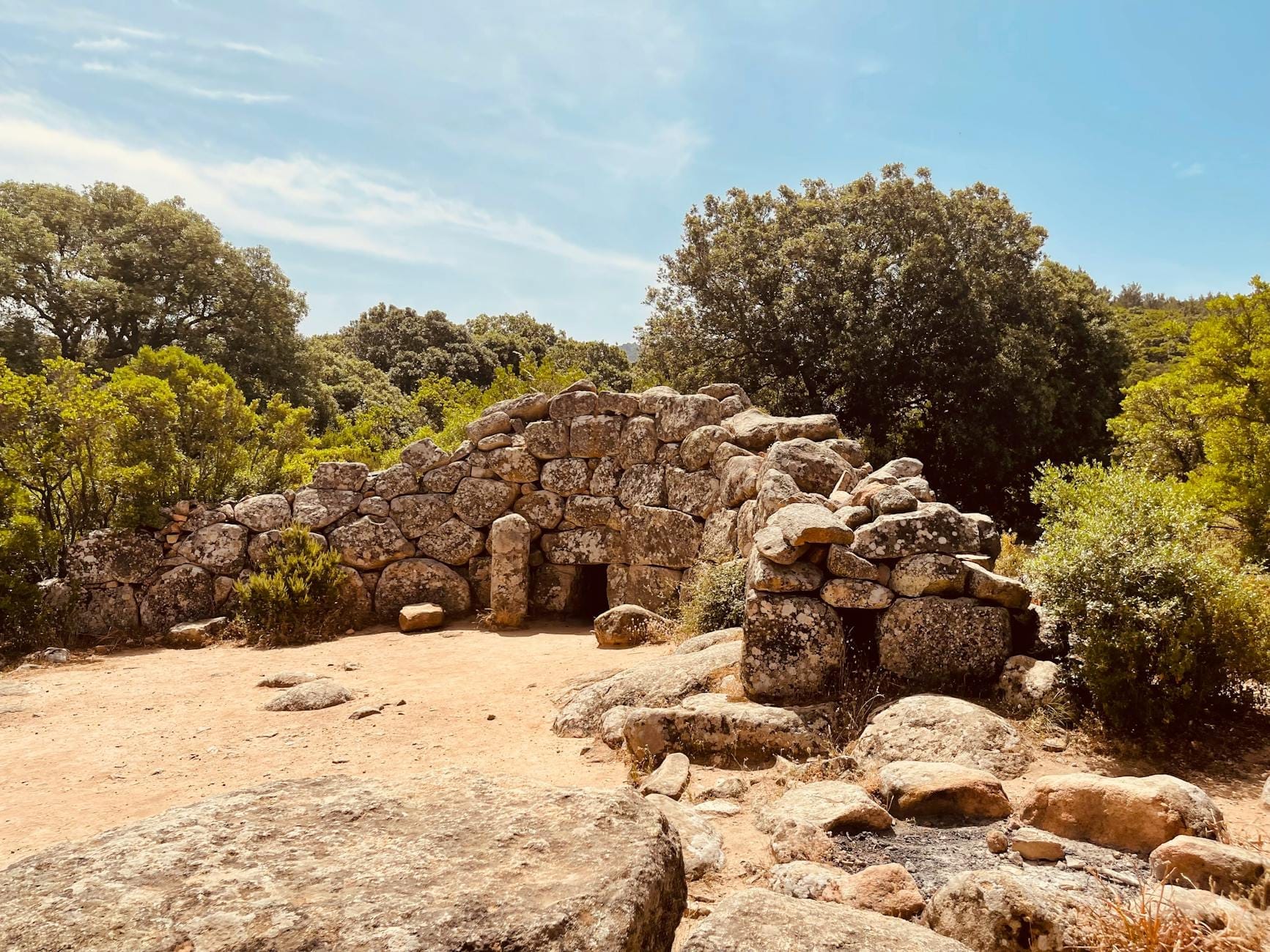 Alte Steinstruktur umgeben von Bäumen und Felsen auf Sardinien, unter einem blauen Himmel