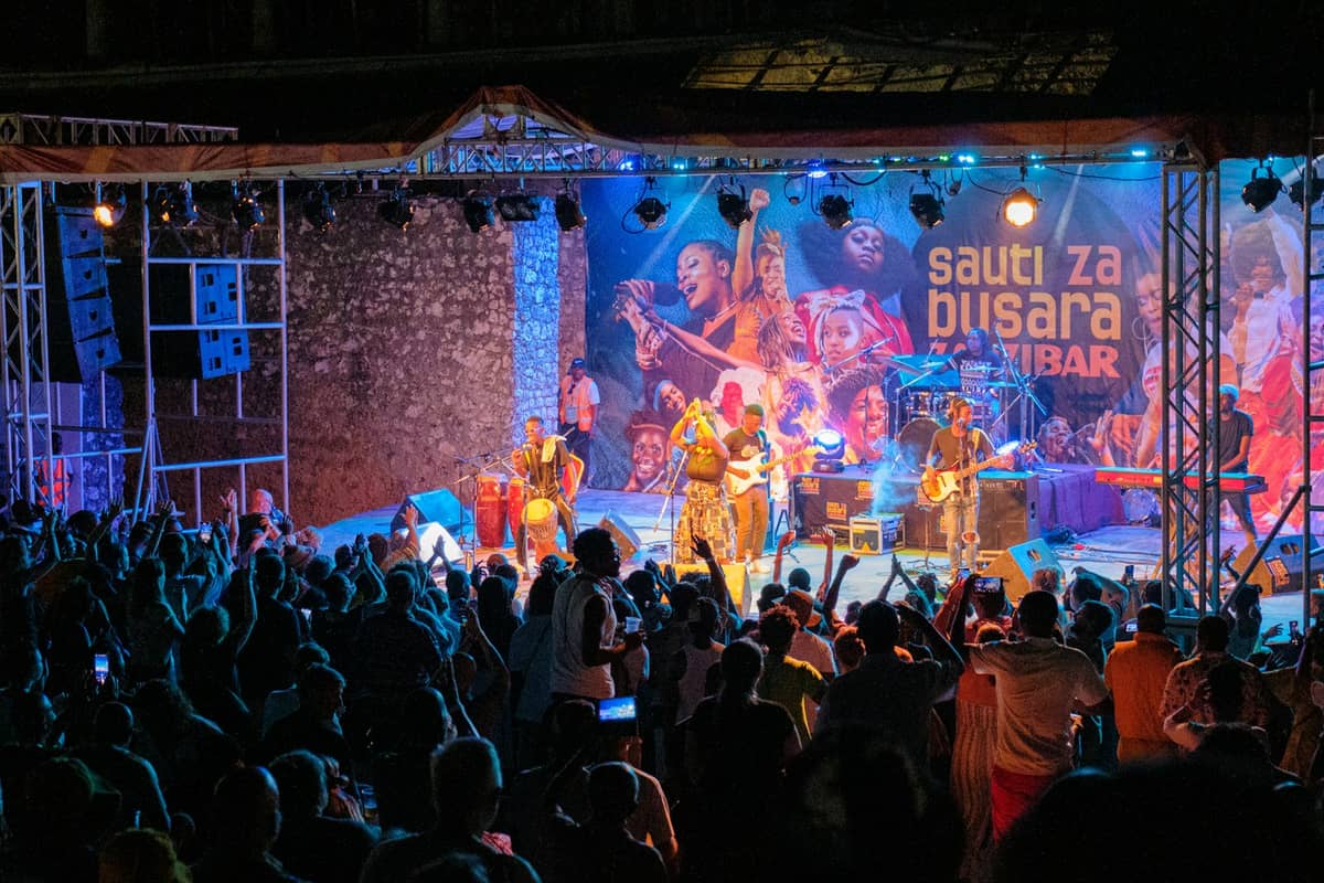 Esibizione notturna sul palco del festival Sauti za Busara: musicisti sotto le luci davanti a una folla festante e allo striscione del festival a Stone Town.