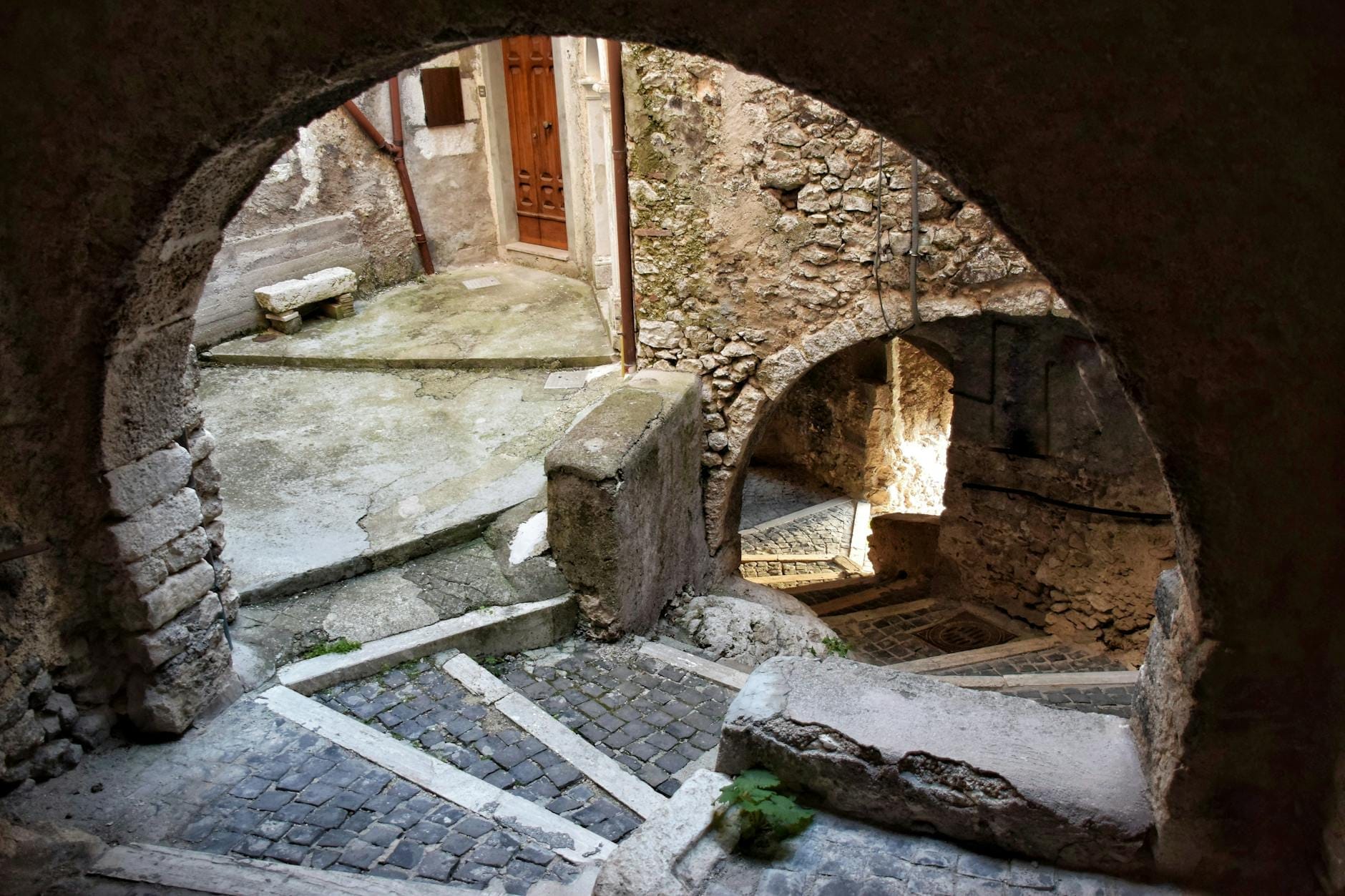 Eine alte Steintreppe schlängelt sich durch Bögen und historische Mauern einer sizilianischen Stadt, in warmes natürliches Licht getaucht.