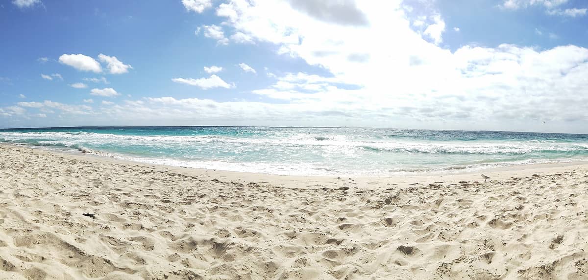 Scarborough Beach mit hellem Sand im Vordergrund, sanften blauen Wellen des Indischen Ozeans und einem teils bewölkten Himmel an einem sonnigen Tag in Perth.