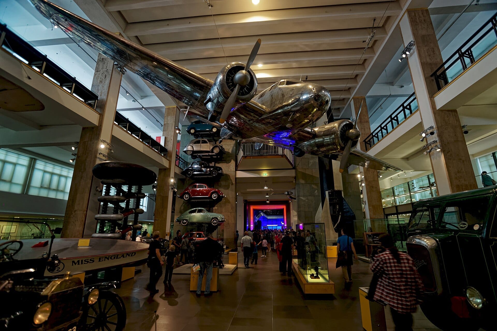All'interno del Science Museum di Londra, i visitatori camminano sotto un grande aereo sospeso, circondati da auto d'epoca e veicoli storici in un'ampia sala.