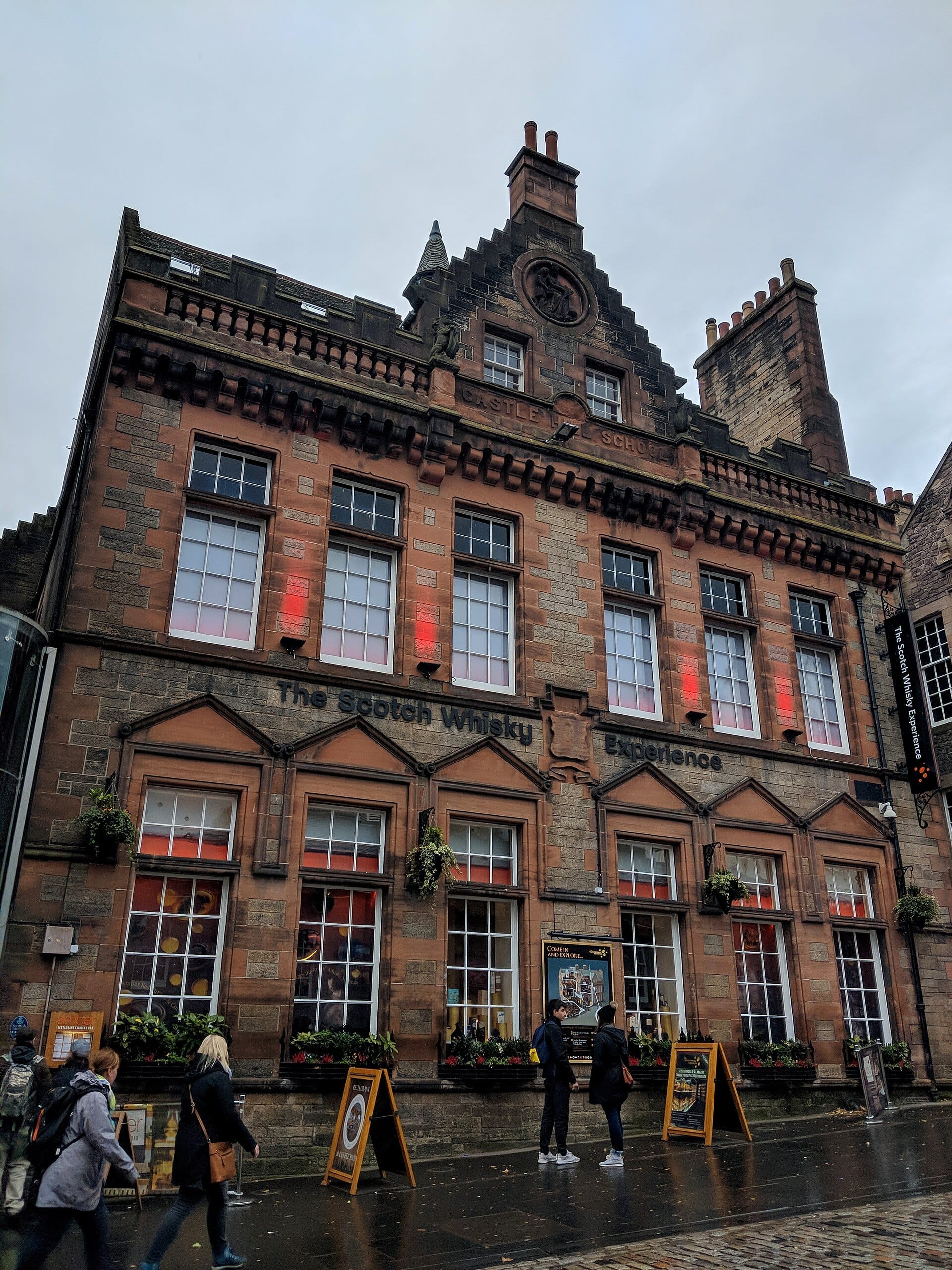 Frontansicht der The Scotch Whisky Experience, einem historischen Steingebäude am Royal Mile in Edinburgh, mit vorbeigehenden Fußgängern an einem bewölkten Tag.
