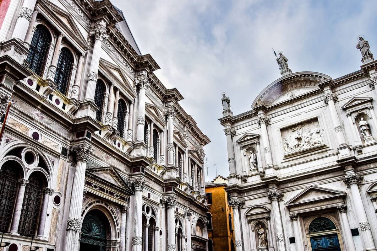 Die prächtige weiße Marmorfront der Scuola Grande di San Rocco in Venedig mit ihren Renaissancedetails, Statuen und Bogenfenstern vor blauem Himmel.