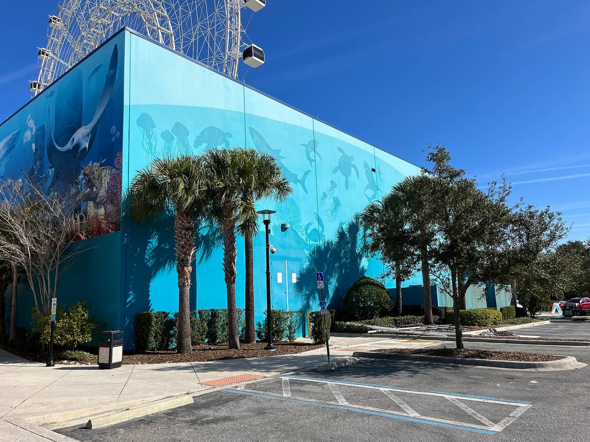 Exterior of SEA LIFE Orlando Aquarium at ICON Park, showing aqua blue building with aquatic murals and palm trees under a clear sky.