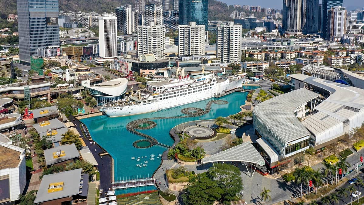 Vista aérea de Sea World Plaza em Shekou, com o navio MV Minghua atracado em uma lagoa turquesa rodeada de edifícios modernos.