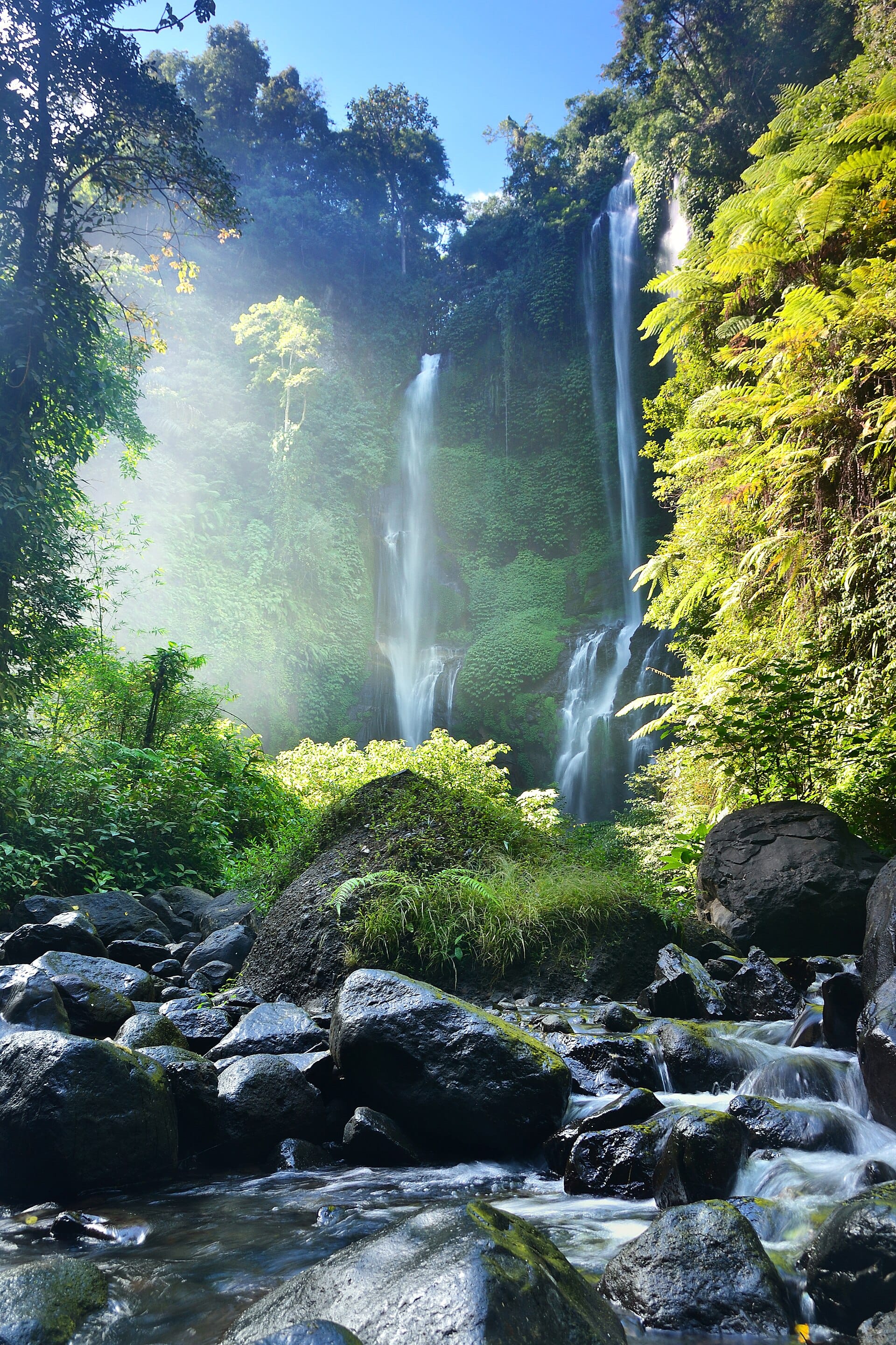 La cascata di Sekumpul, la più alta di Bali, con due potenti getti d'acqua che precipitano tra le rigogliose valli del nord dell'isola e una lussureggiante vegetazione verde scuro.