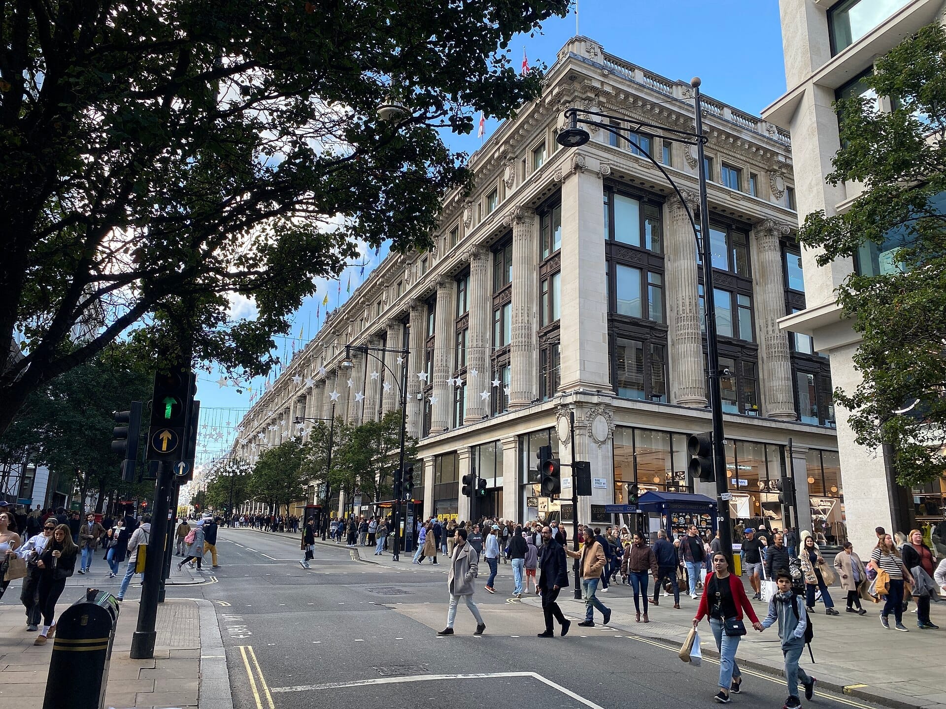 La grandiosa facciata di Selfridges London su una trafficata Oxford Street, con folle di acquirenti che attraversano sotto cieli azzurri limpidi.