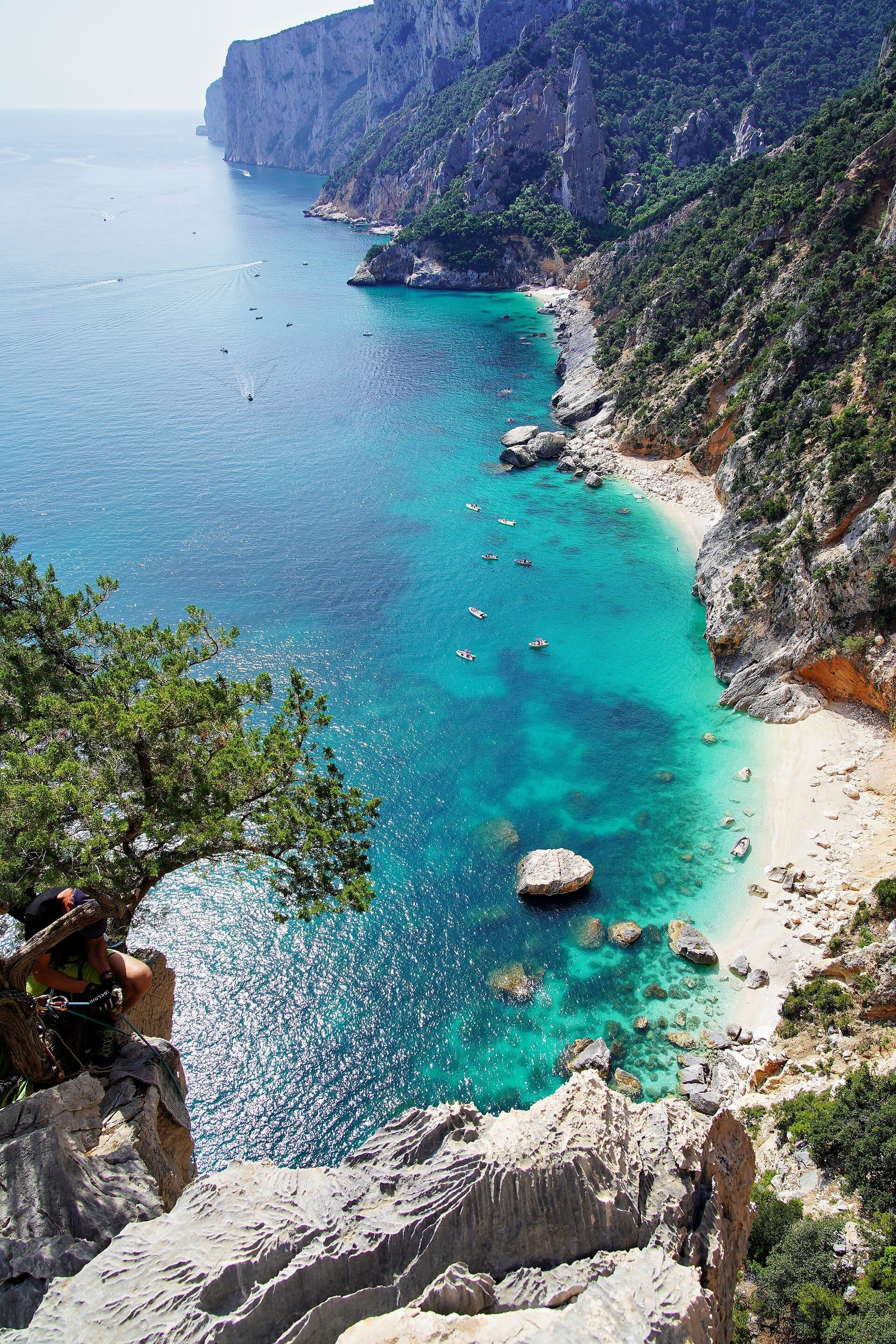 Dramatischer Blick von hohen Klippen auf das türkisfarbene Wasser und die zerklüftete Kalksteinküste des Selvaggio Blu Trekkingpfades an der Ostküste Sardiniens.