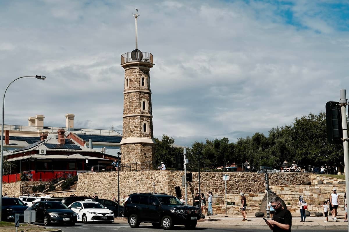 ประภาคารหินประวัติศาสตร์ของ Semaphore ตั้งตระหง่านอยู่ใต้ท้องฟ้าที่มีเมฆบางส่วน ล้อมรอบด้วยผู้คน รถยนต์ ต้นไม้ใบหนาแน่น และอาคารใกล้เคียงที่มีหลังคาสีแดง