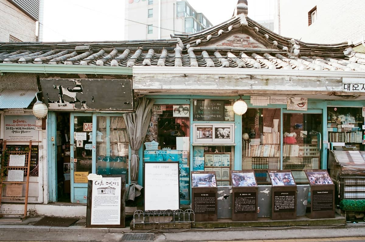 Livraria hanok tradicional com acabamentos azuis rústicos e placas escritas à mão em Seochon Village, Seul, numa tranquila rua urbana.