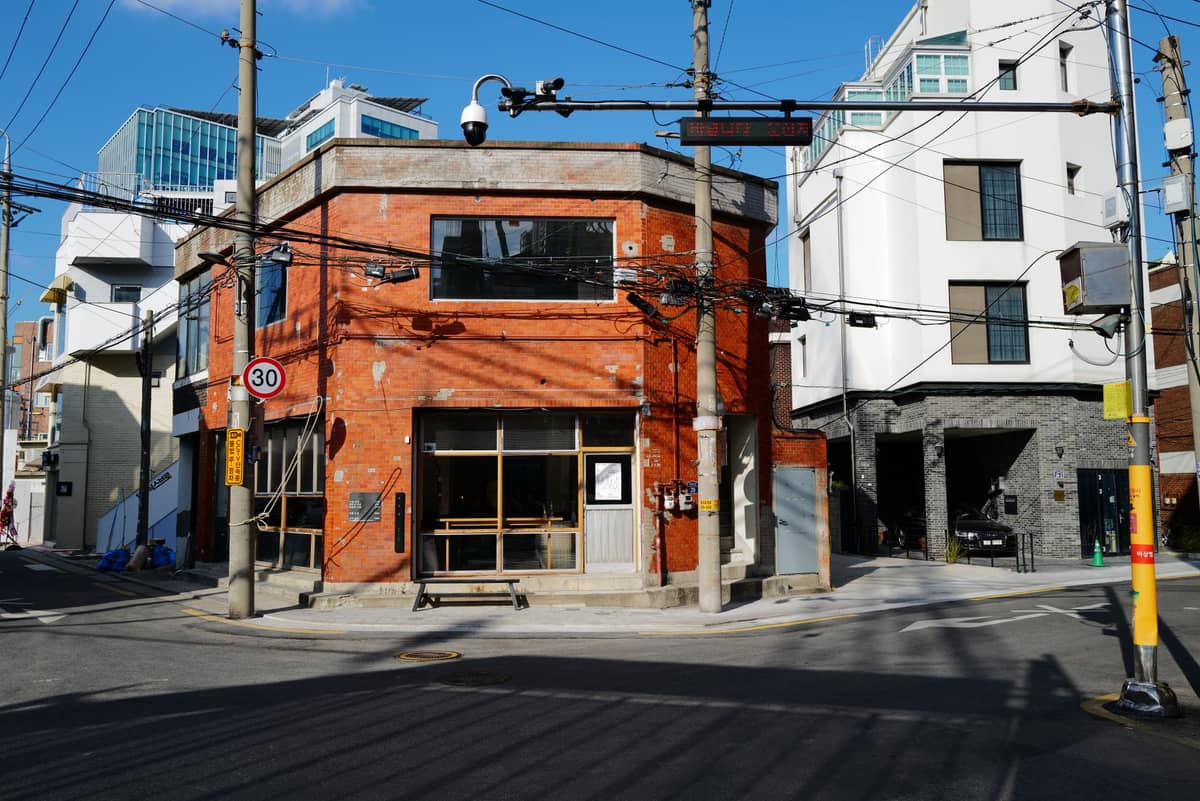Um edifício estilo armazém de tijolos que abriga um café em uma esquina ensolarada em um bairro de Seul com visual industrial e moderno.