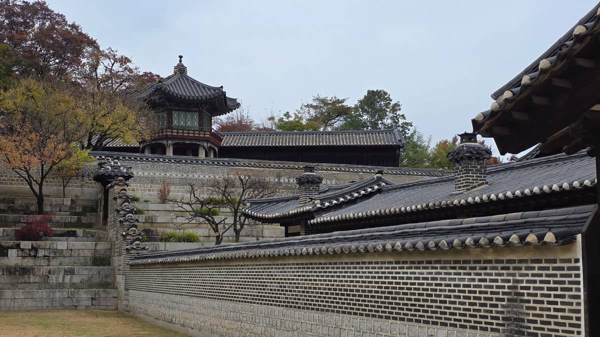 Pavilhões coreanos tradicionais e muros de pedra com telhas rodeados de árvores com folhagem outonal no Jardim Secreto do Palácio Changdeokgung em Seul.
