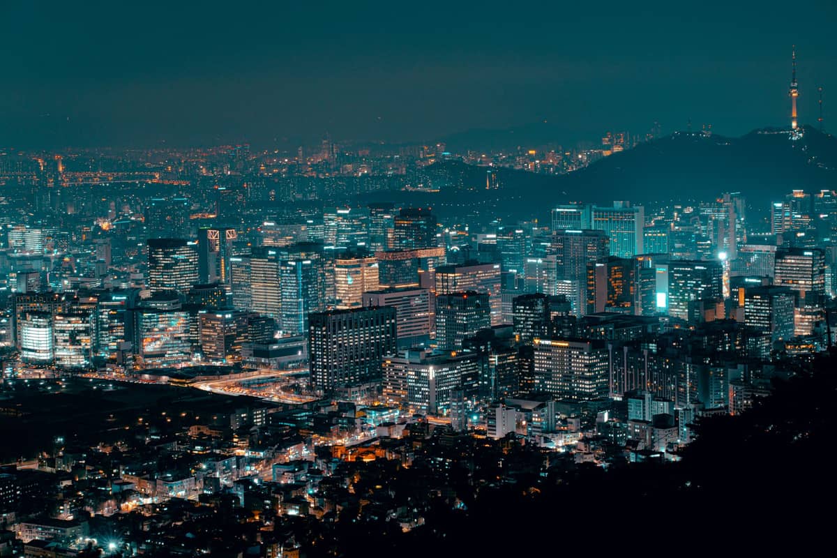 Panorama noturno do horizonte de Seul com a Namsan Seoul Tower e edifícios iluminados, mostrando uma paisagem urbana vibrante e moderna.