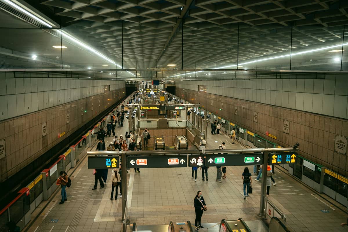 Vista ampla de uma movimentada plataforma de metrô em Seul com sinalização clara, passageiros aguardando, paredes de azulejos e escadas rolantes, ilustrando o sistema de metrô limpo e moderno da cidade.
