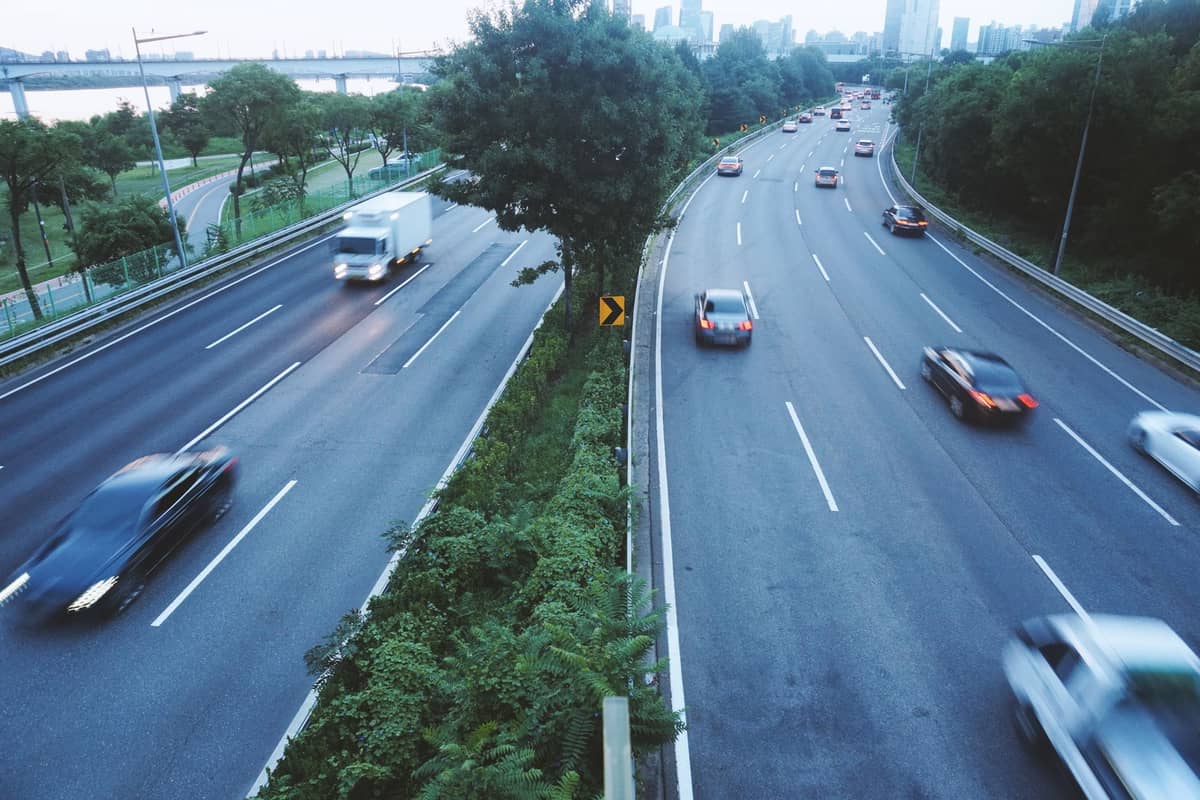 Ampla rodovia em Seul com carros trafegando em ambas as direções, o horizonte da cidade ao fundo e árvores ao longo da estrada