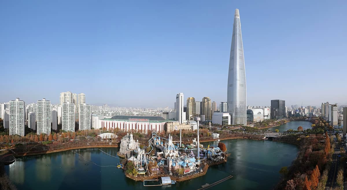 Vista panorâmica de Lotte World em Seul mostrando o edifício do parque temático interno, Magic Island no lago e a Lotte World Tower ao fundo.