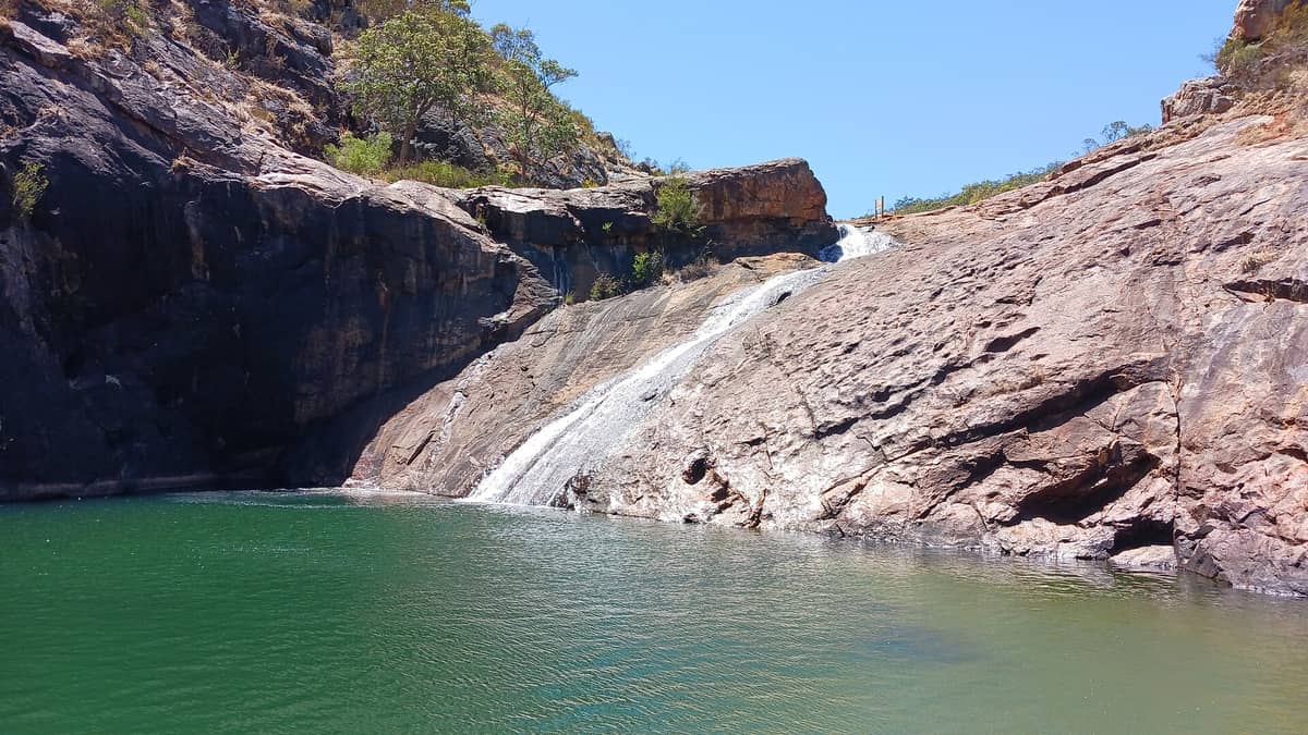 Die Serpentine Falls stürzen über glatte Granitsteine in ein natürliches Schwimmloch, umgeben von schroffen Felsen und einem klaren blauen Himmel.