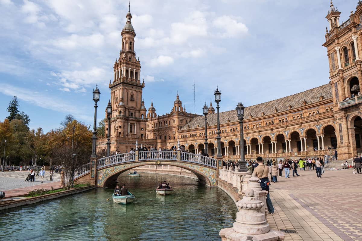 Plaza de España ในเซบียายามฤดูใบไม้ร่วงกับสถาปัตยกรรมโดดเด่น หอคอยกลาง ลำคลองมีเรือพาย และผู้คนเดินเล่นในจัตุรัส