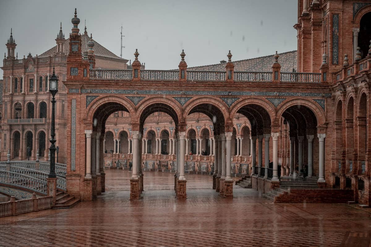 Plaza de España ในเมือง Seville ในวันที่ฝนตกและเงียบสงัด พื้นกระเบื้องเปียกชื้นและท้องฟ้าครึ้ม สะท้อนบรรยากาศเดือนพฤศจิกายนที่เงียบงันและชุ่มชื้น