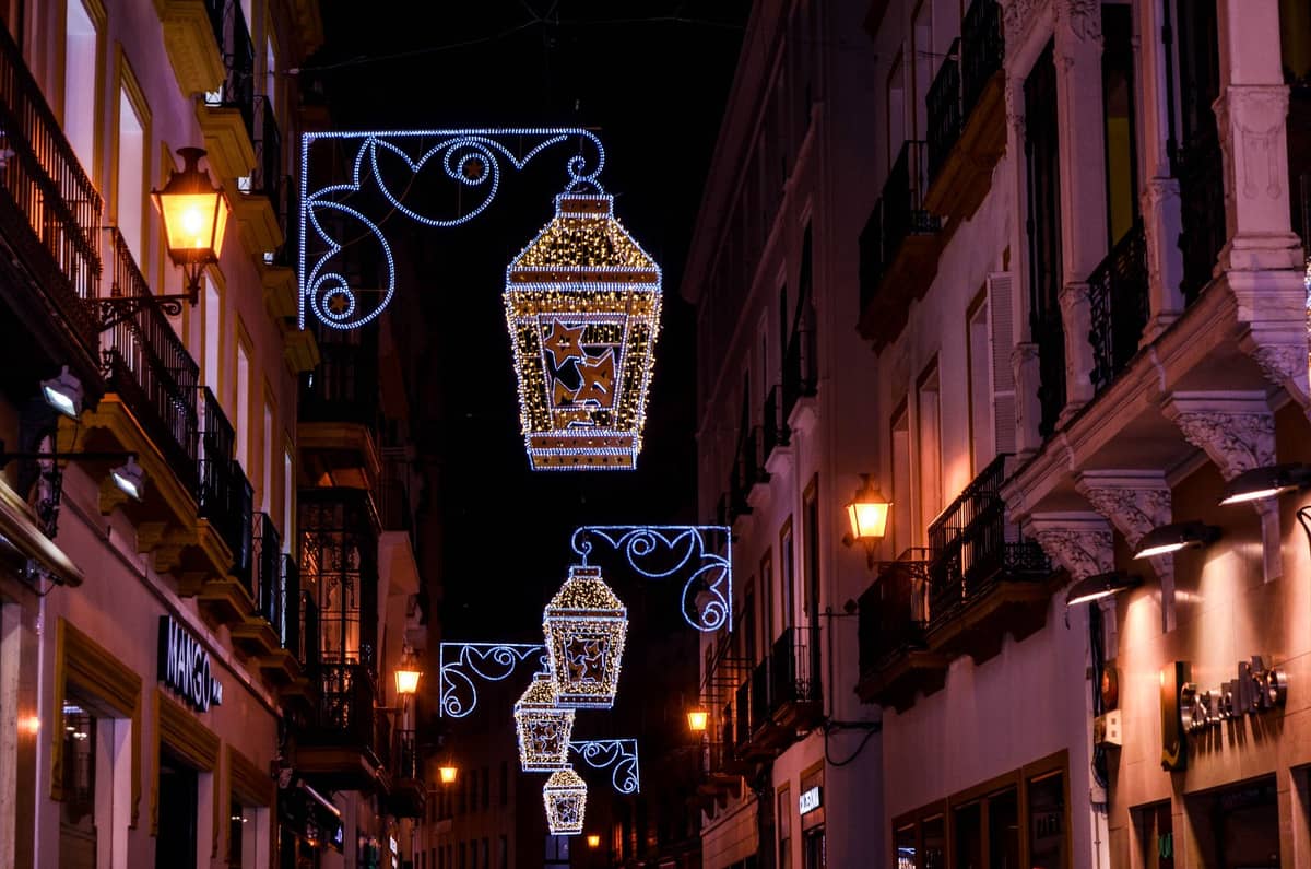ถนนแคบในเมือง Seville ยามค่ำคืนตกแต่งด้วยโคมไฟประดับประดาสวยงาม เรียงรายด้วยอาคารแบบดั้งเดิมและแสงไฟร้านค้าที่เปล่งประกาย