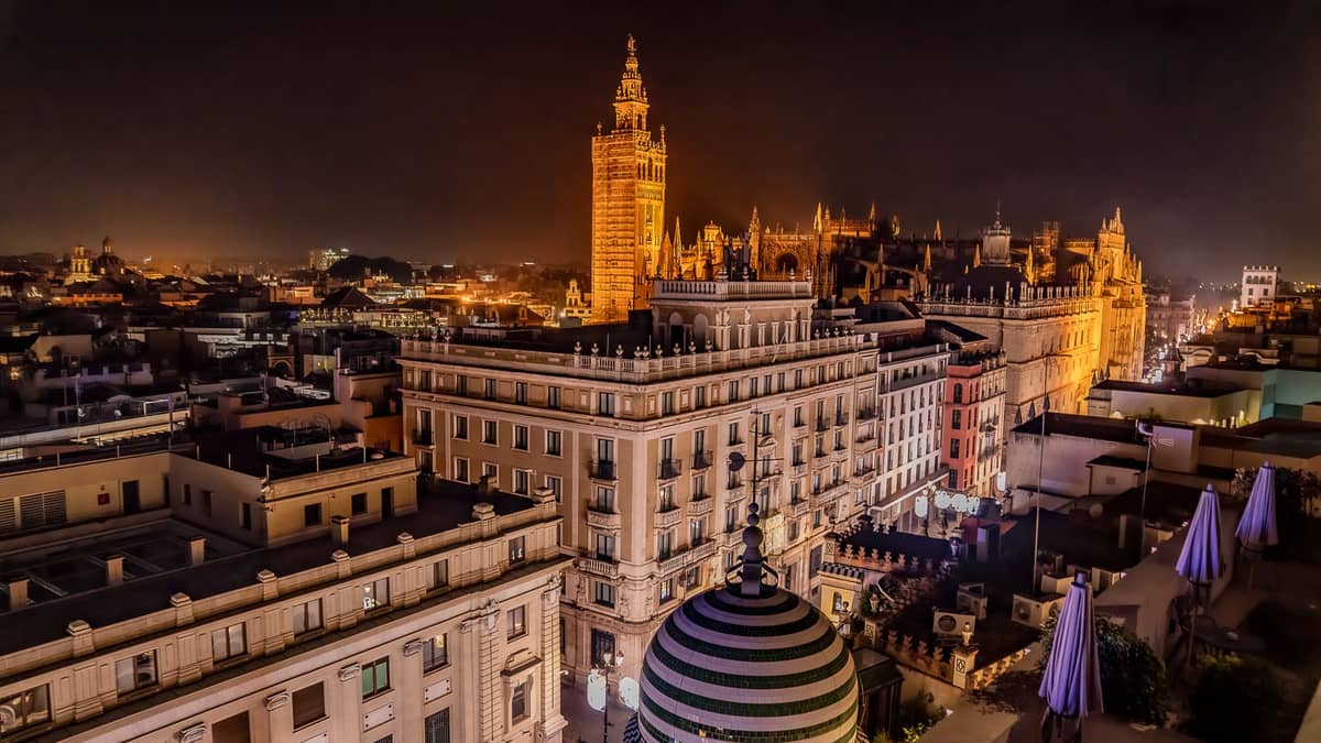 เซบียายามค่ำคืน มุมสูงเห็นใจกลางเมือง หอคอย Giralda โบสถ์โดดเด่นด้วยแสง พร้อมบรรยากาศ rooftops สุดครื้นเครงเบื้องหน้า