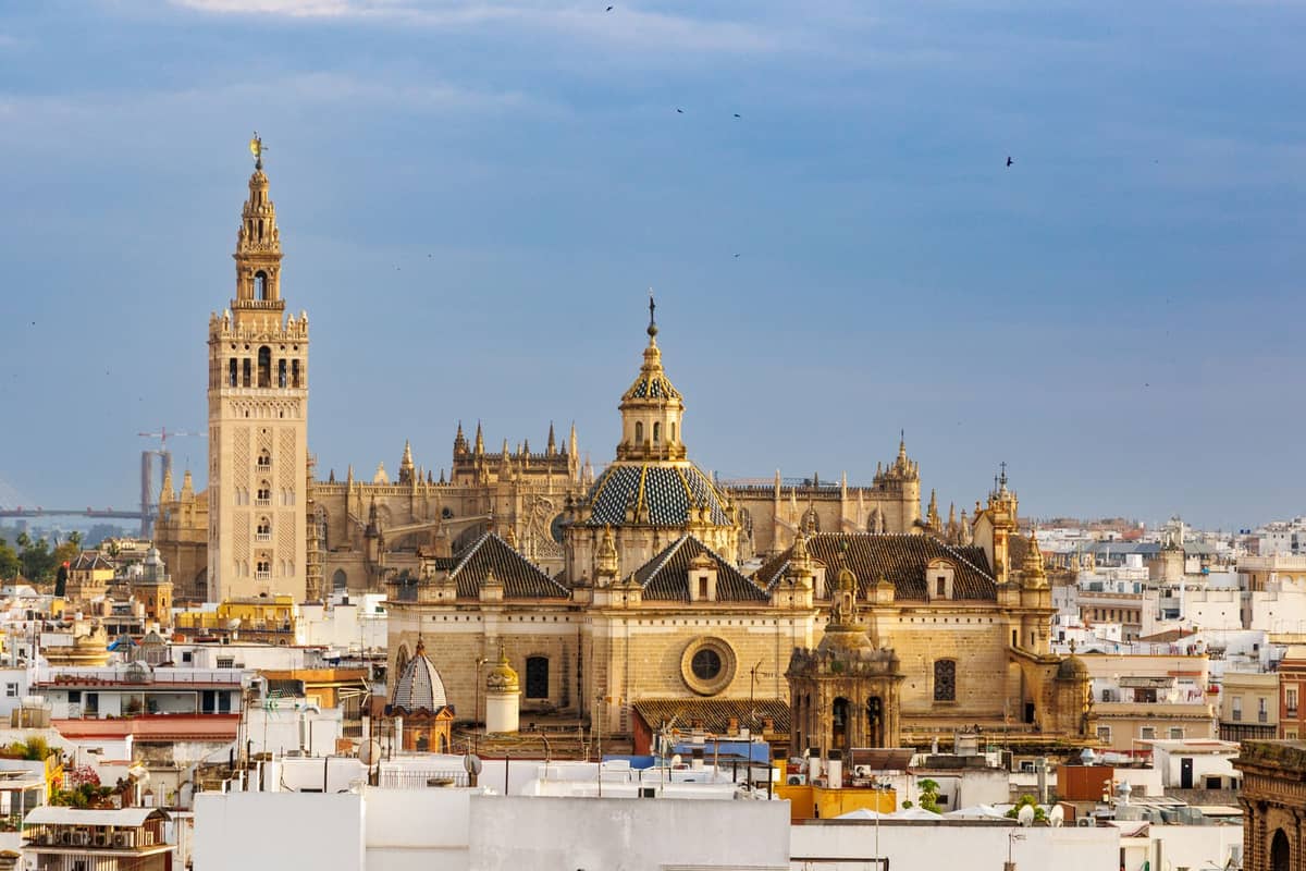 Panoramic view of Seville’s famous cathedral and Giralda tower rising above the city’s rooftops under a blue sky, capturing the city’s iconic historic skyline.