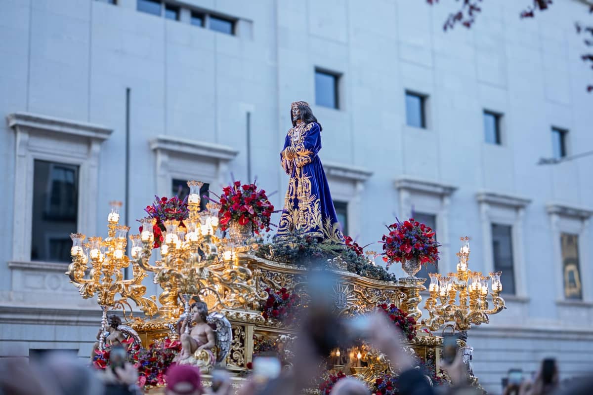 ภาพระยะใกล้ของแท่นแห่ทางศาสนา Semana Santa พร้อมรูปปั้นและการตกแต่งทองคำอันวิจิตร ล้อมรอบด้วยฝูงชนในเมือง Seville