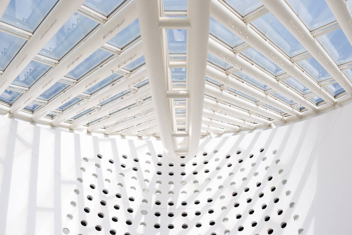 L'atrio luminoso dell'SFMOMA con un lucernario di vetro geometrico e travi bianche che proiettano ombre su una parete interna perforata di bianco.