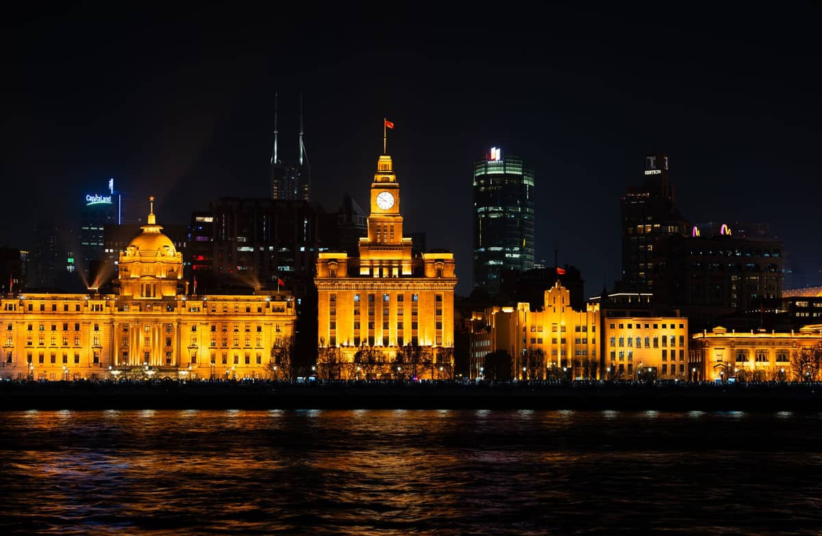 Nächtliche Ansicht des Bund in Shanghai, mit beleuchteten Gebäuden aus der Kolonialzeit entlang der Uferpromenade und modernen Wolkenkratzern im Hintergrund.