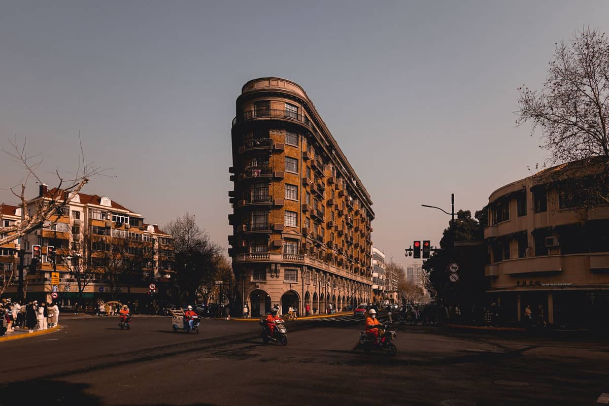 Markante Ansicht der historischen Normandie Apartments, einem ikonischen Art-Déco-Gebäude an der Wukang Road in Shanghai, mit einer keilförmigen Fassade und Straßenszene.