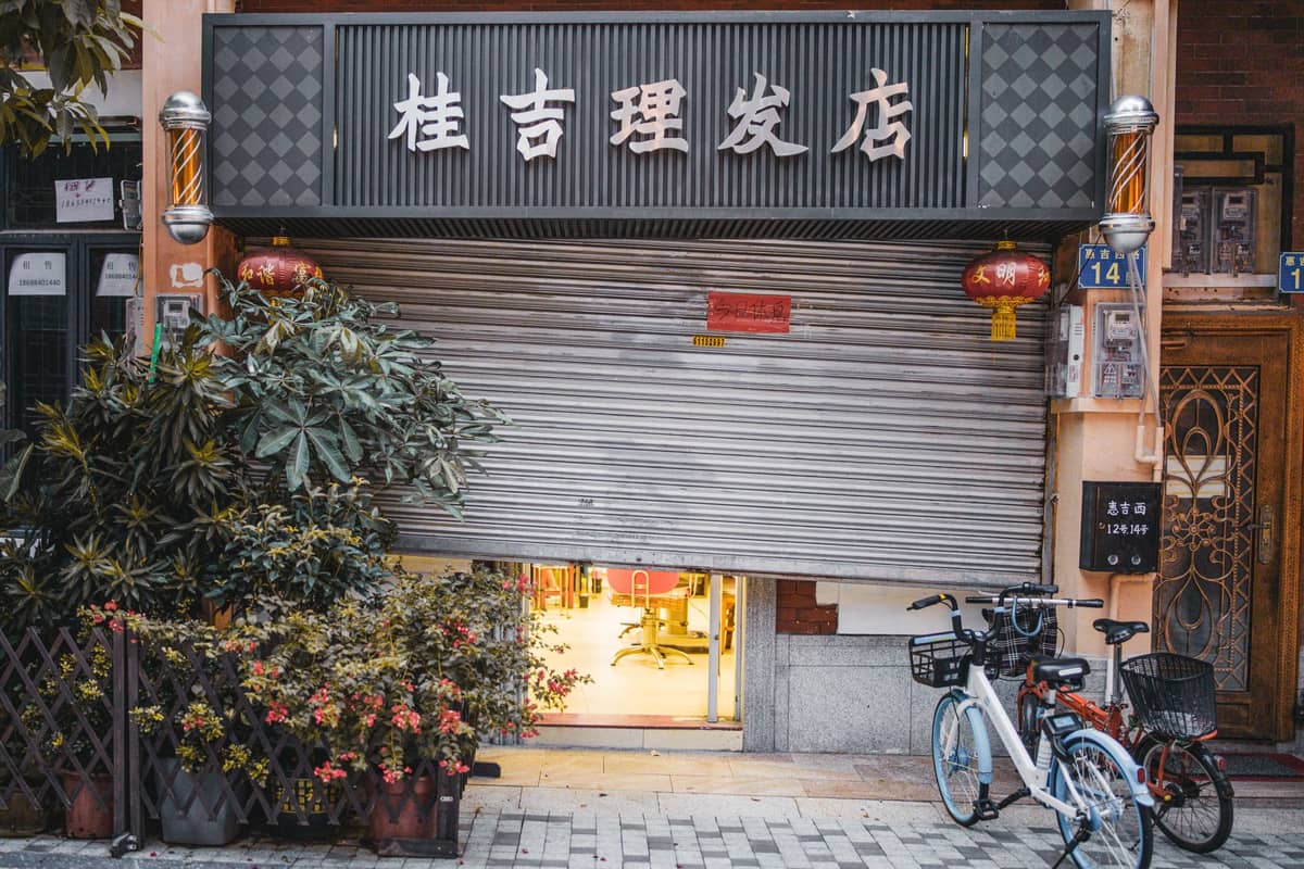 Un negozio in una città cinese con la saracinesca metallica parzialmente abbassata, due biciclette parcheggiate davanti e lanterne appese all'ingresso.