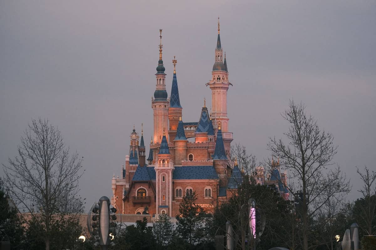 Das Enchanted Storybook Castle im Shanghai Disney Resort am Abend – sanft beleuchtet, eingerahmt von Bäumen im Vordergrund.