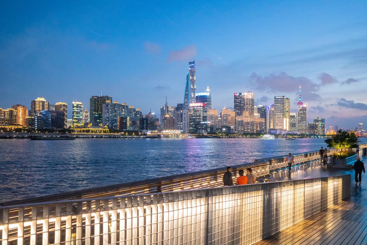 Abendliche Aussicht von der Uferpromenade The Bund in Shanghai mit Menschen am Flussufer und der beleuchteten Skyline von Pudong auf der anderen Seite des Huangpu.