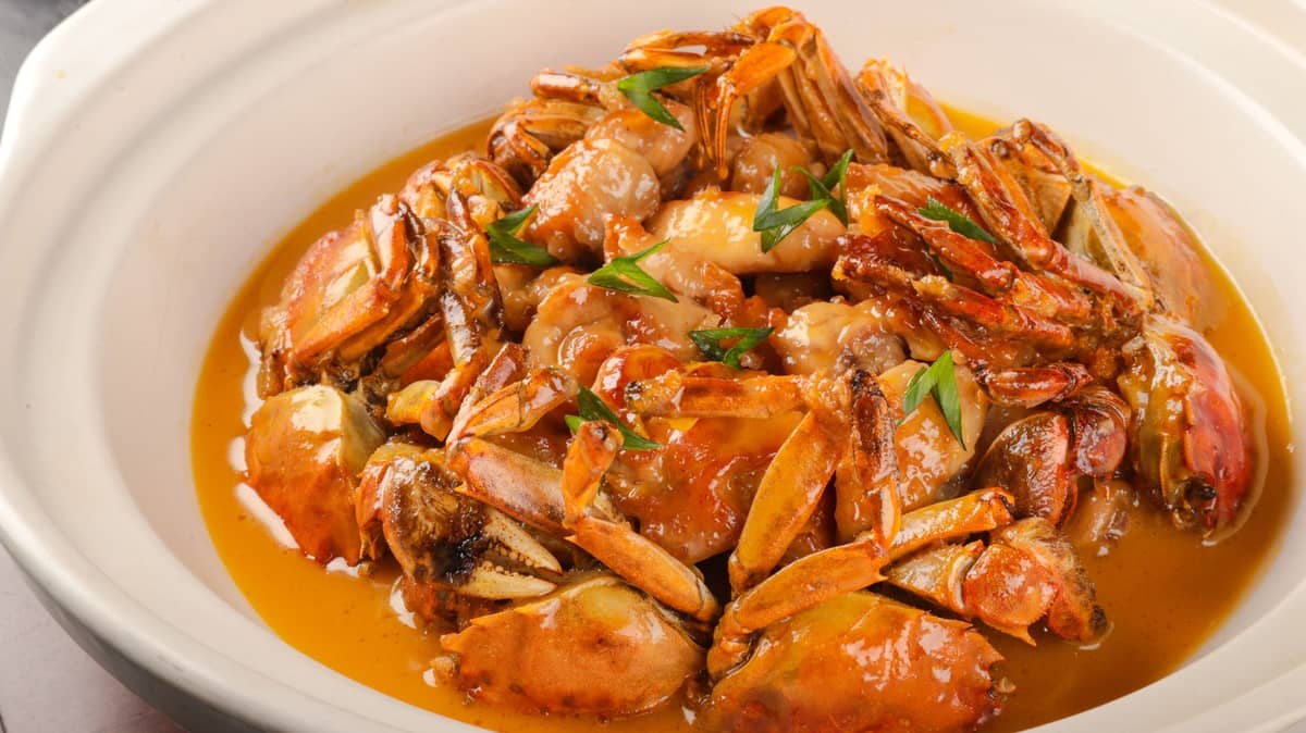 Eine große Schüssel gegarter Haariger Krabben nach Shanghaier Art, in reichhaltige orangefarbene Sauce getaucht und mit frischen Frühlingszwiebeln garniert.