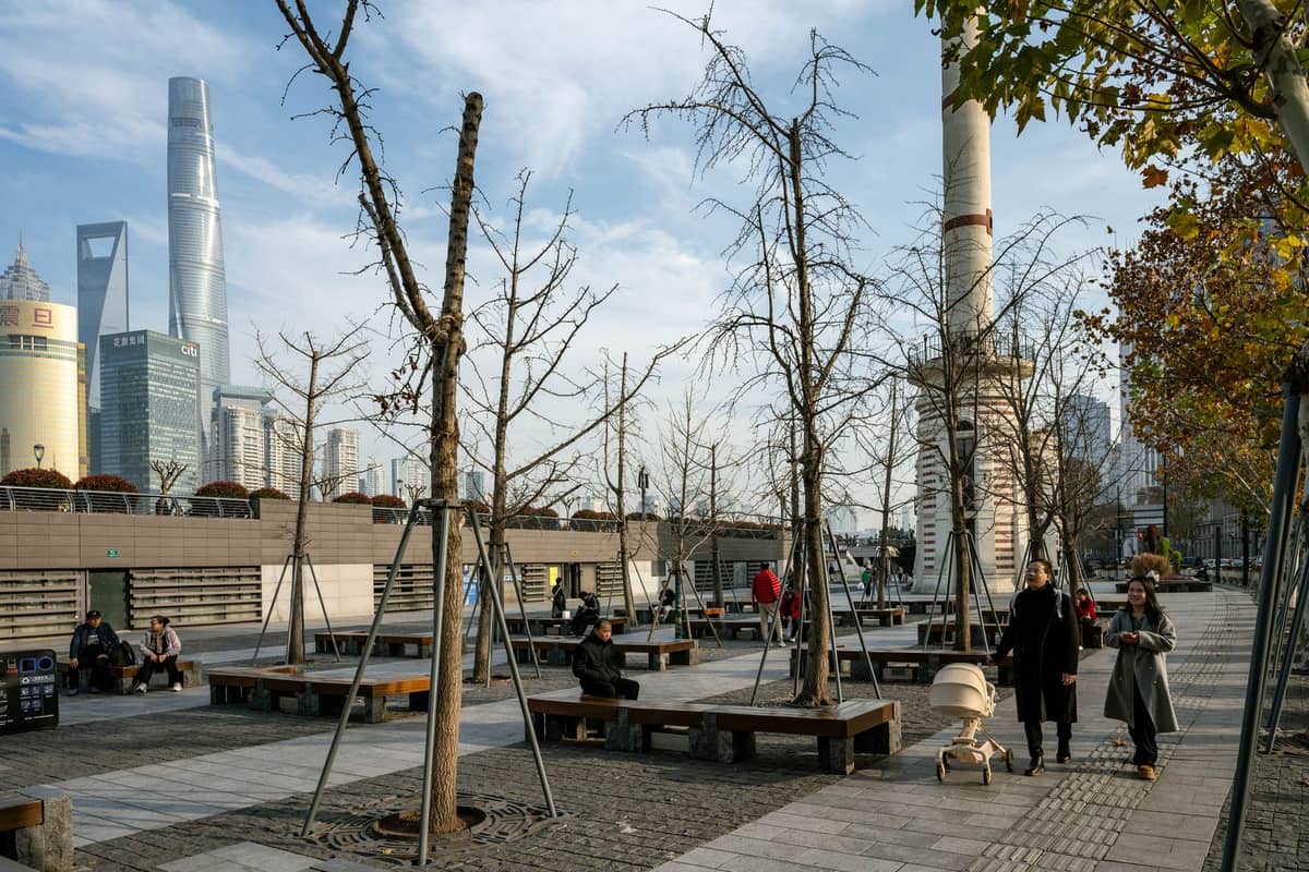 Des personnes se promenant et se détendant sur une promenade moderne au bord de la rivière à Shanghai, avec des gratte-ciel et des arbres d'automne en arrière-plan.